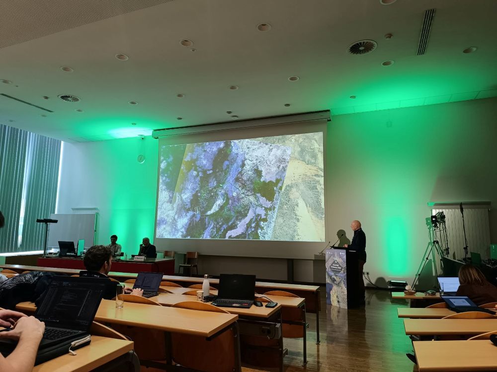 mężczyzna z mikrofonem w ręce podczas prelekcji, na tle ekranu