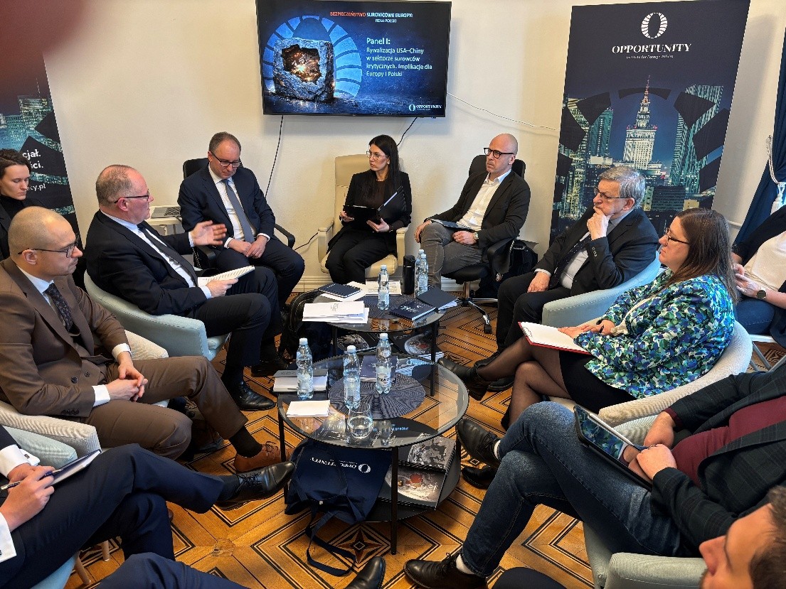 grupa osób siedząca na sali przy stole i prowadzących rozmowę ze sobą