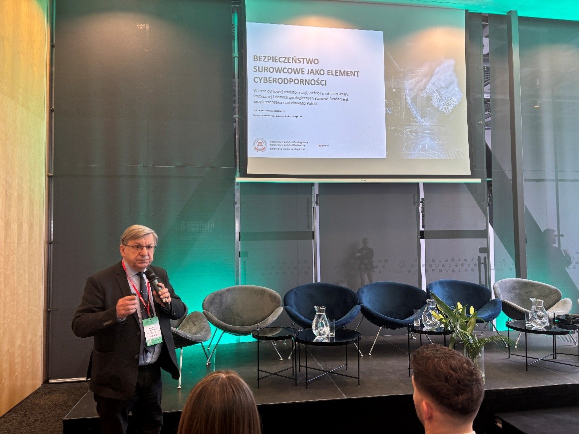 mężczyzna z mikrofonem w ręce podczas prelekcji, na tle ekranu