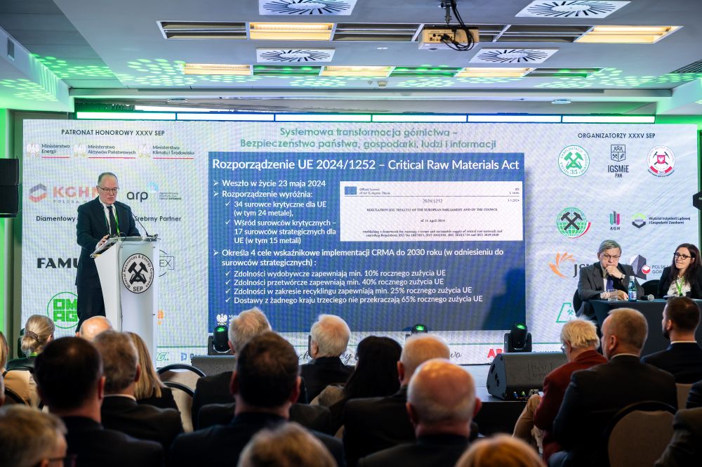 mężczyzna z mikrofonem w ręce podczas prelekcji, na tle ekranu