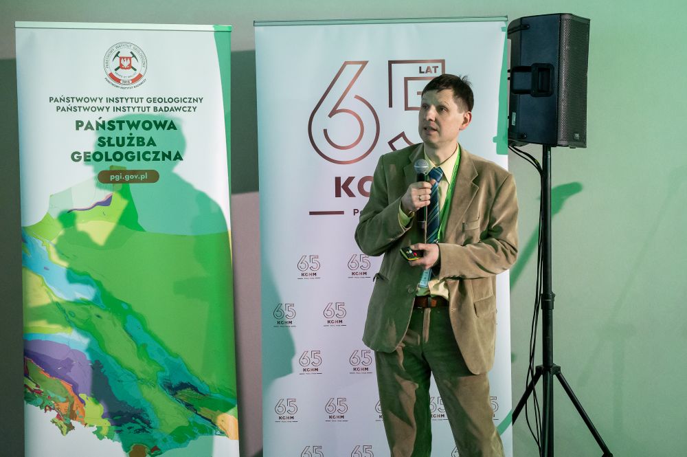 mężczyzna z mikrofonem w ręce podczas prelekcji, na tle ekranu