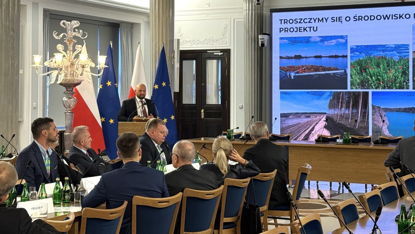 mężczyzna przemawia do siedzącej w pomieszczeniu publiczności