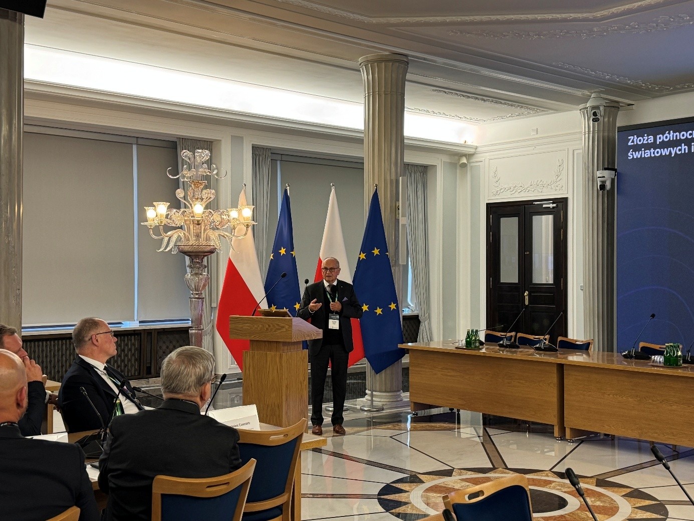 mężczyzna przemawia do siedzącej w pomieszczeniu publiczności